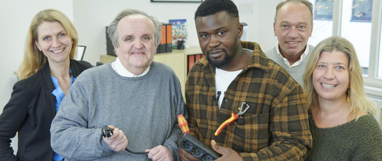 Fünf Personen mit Steckerleiste in den Händen stehen in einem Büro.