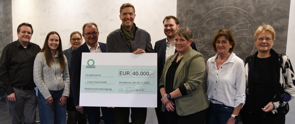 Eine Personengruppe mit einem symbolischen Scheck steht in einem Foyer.