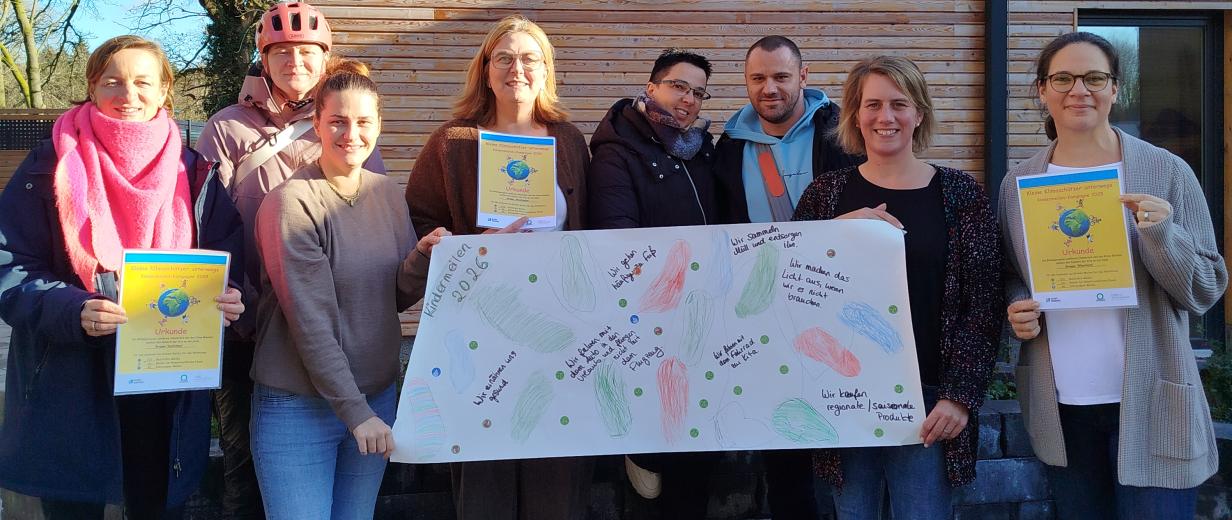 Eine Personengruppe mit Plakaten in den Händen steht vor einem Haus mit Holzfassade.