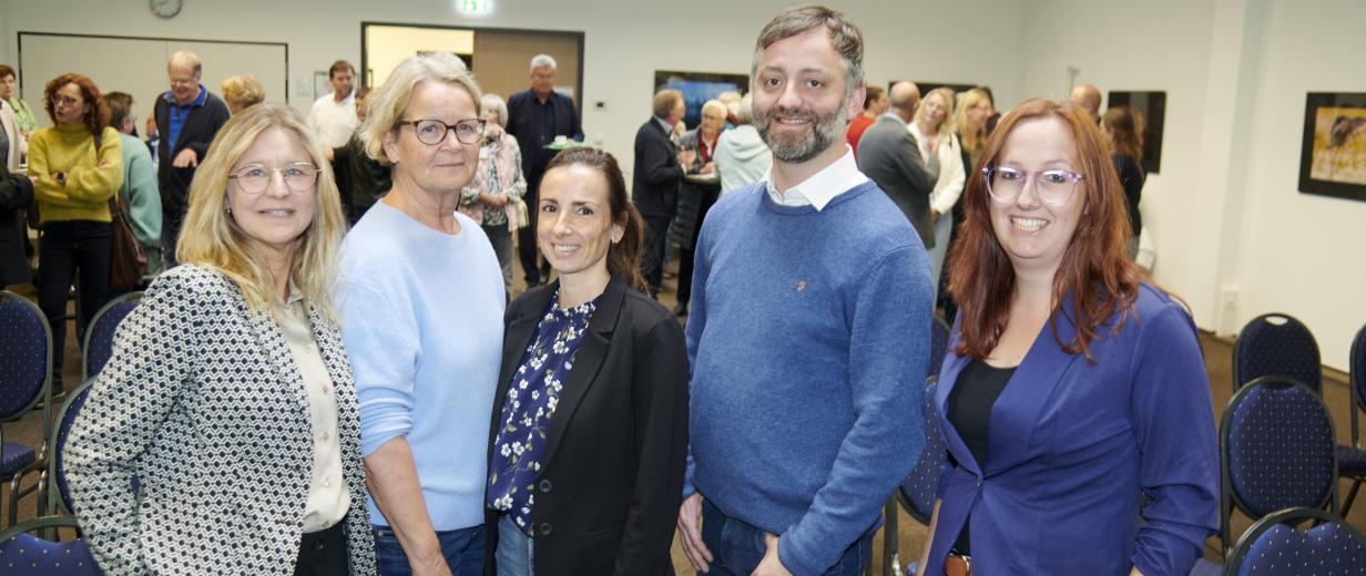 Fünf Personen stehen nebeneinander in einem Raum.