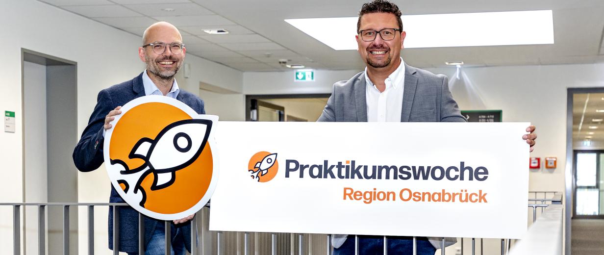 Zwei Personen mit Pappschild stehen in einem Treppenhaus.