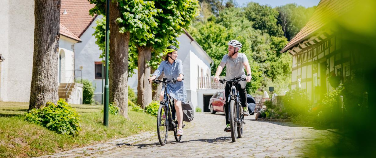Zwei Personen auf Fahrrädern auf einer Dorfstraße.