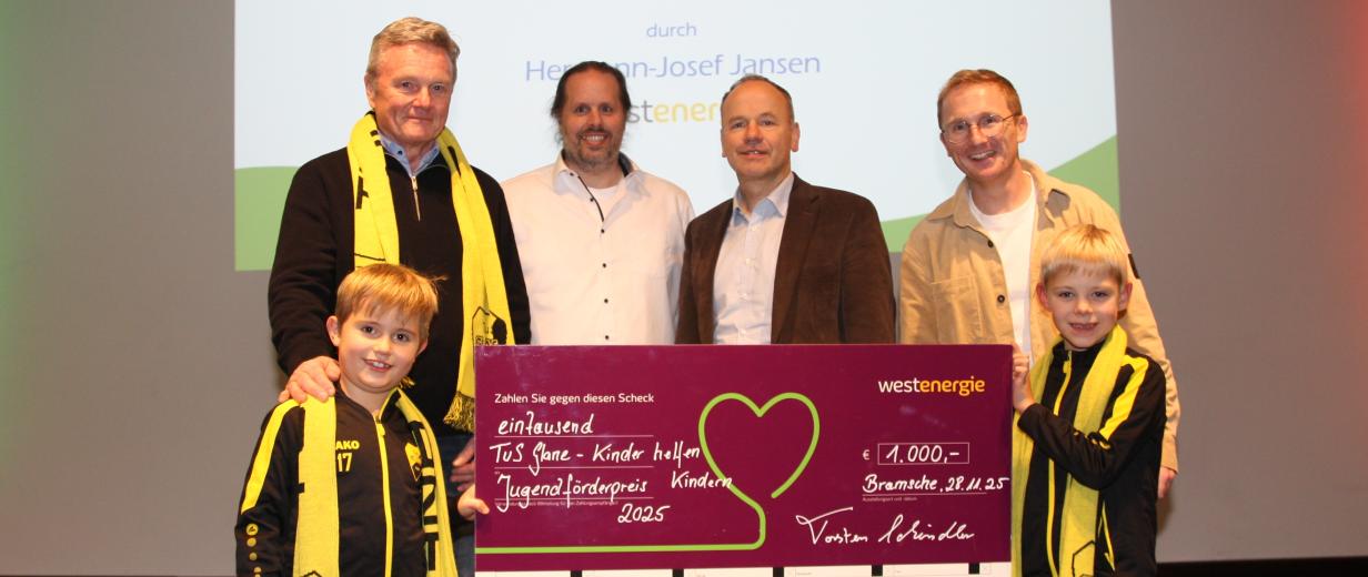 Sechs Personen mit einem symbolischen Scheck stehen auf einer Bühne.