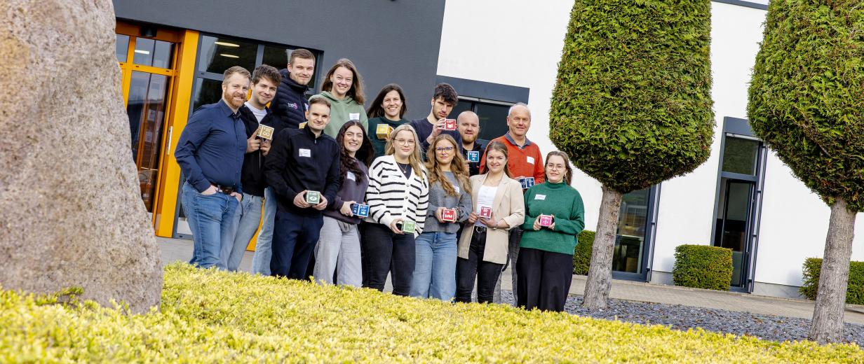 Eine Personengruppe steht vor einem Firmengebäude.