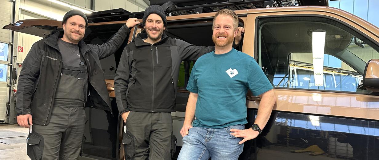 Drei Personen stehen vor einem Wohnmobil in einer Werkhalle.