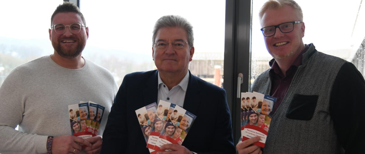 Drei Personen Stehen im Gegenlicht vor einer Glasfassade.