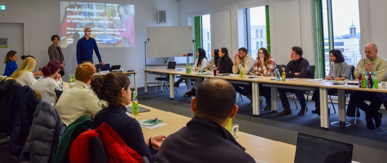 Seminarraum mit einer Personengruppe, die einem Referenten zuhört.