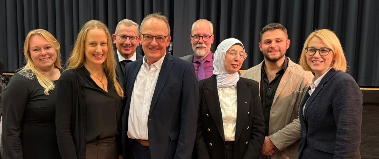 Eine Personengruppe steht vor einem Vorhang.