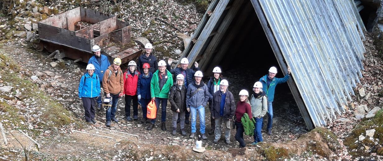 Personengruppe mit Helmen steht am Eingang zu einem Stollen.