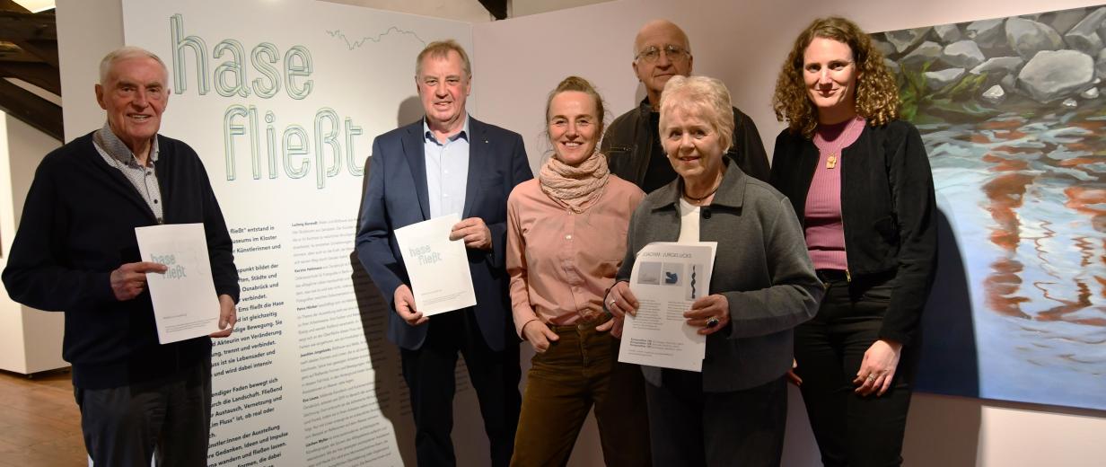 Sechs Personen stehen in einer Ausstellung nebeneinander.