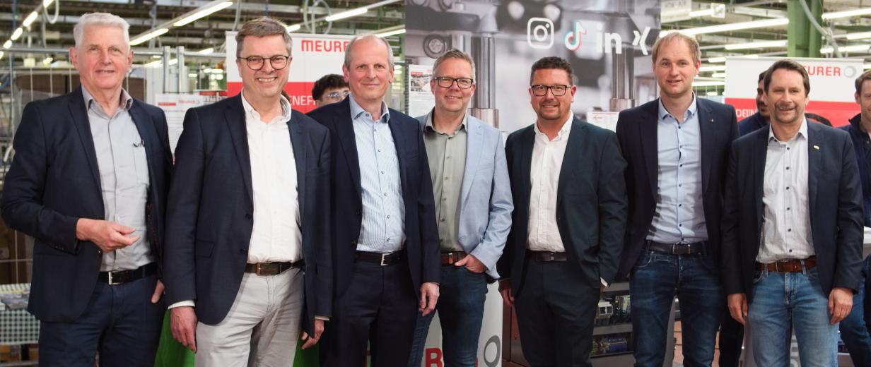 Sieben Personen stehen in einer Werkhalle.