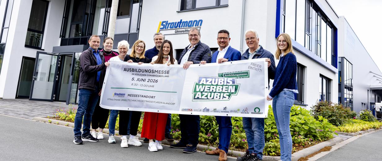 Personengruppe mit einem Banner steht vor einem Bürogebäude