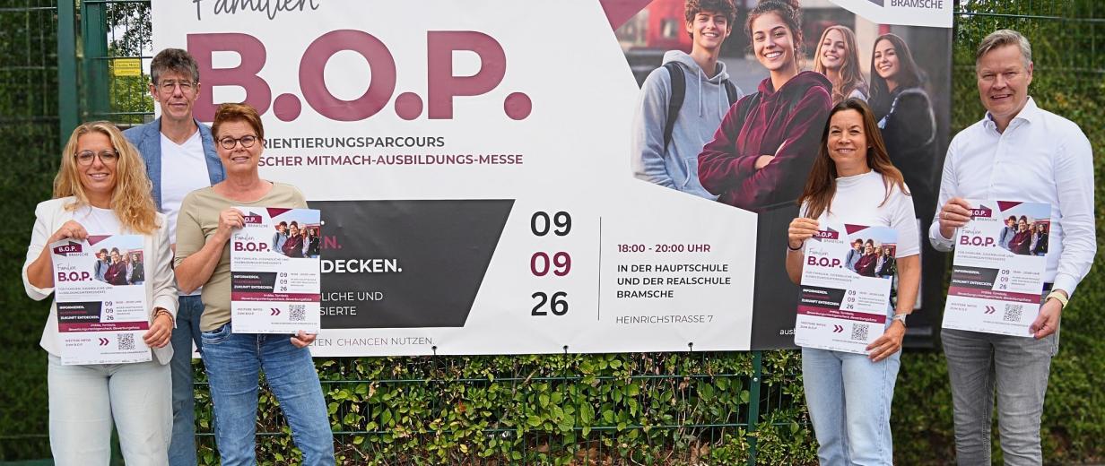 Fünf Personen stehen vor einem Zaun, an dem ein Plakat befestigt ist.