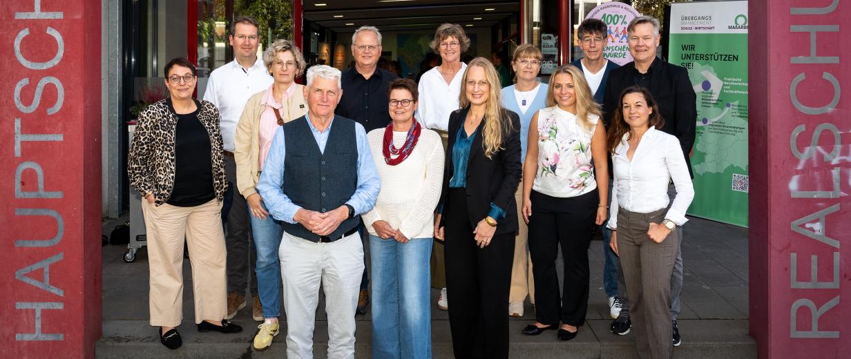Personengruppe steht vorm Eingang eines Schulgebäudes
