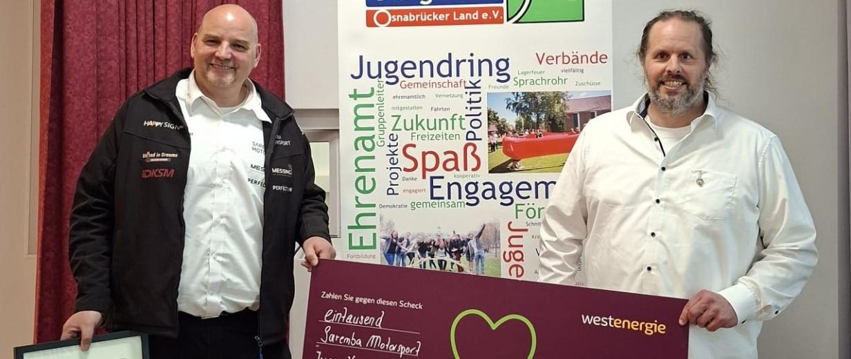 Zwei Personen mit Urkunde und symbolischem Scheck
