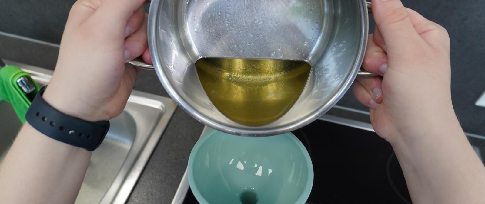 Öl wird aus einem Topf in eine Flasche mit Trichter gegossen.