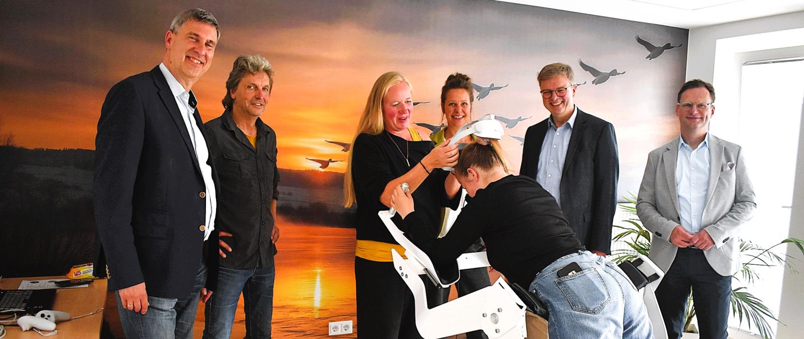 Eine Personengruppe steht in einem Raum vor einem Flugsimulator.