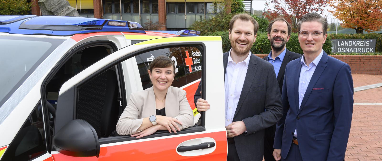 Vier Personen stehen an einem Blaulicht-Fahrzeug.