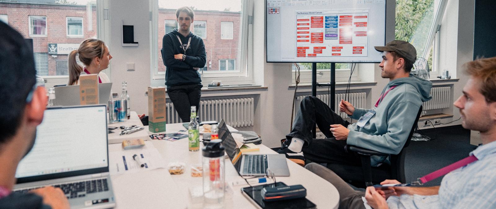 Vier Personen sitzen um einen Besprechungstisch herum, eine steht.