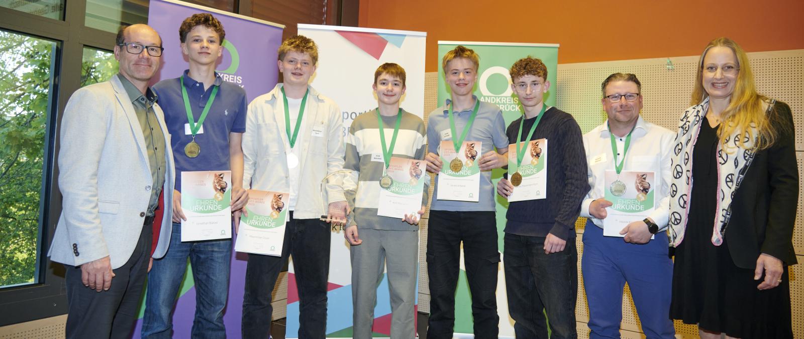 Personengruppe mit Medaillen und Urkunden steht vor Rollup Postern