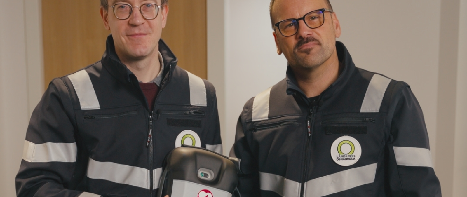 Zwei Personen in Uniformjacken mit einem Defibrillator