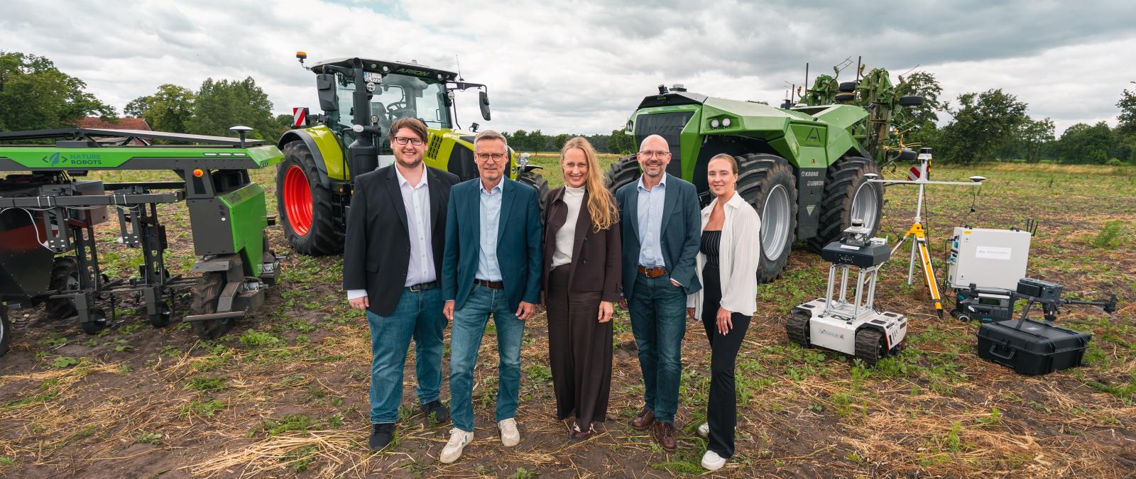 Fünf Personen stehen auf einem Acker vor Landmaschinen.