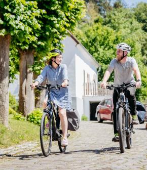 Zwei Personen auf Fahrrädern auf einer Dorfstraße.