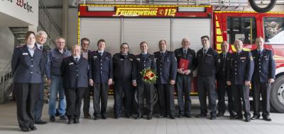 Eine Personengruppe in dunkelblauen Uniformen steht vor einem Feuerwehrfahrzeug.