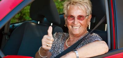 Eine Seniorin sitz in einem Auto, schaut zur Seite und hebt den rechten Daumen.