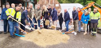 Eine Personengruppe mit Spaten steht hinter einem Sandhaufen.