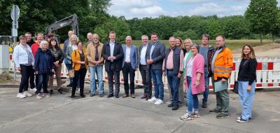 Eine Personengruppe steht vor der Absperrung einer Straßenbaustelle