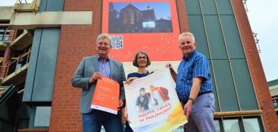 3 Personen halten ein Werbeplakat