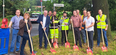 Eine Personengruppe mit schaufeln in den Händen steht an einer Straßenbaustelle.