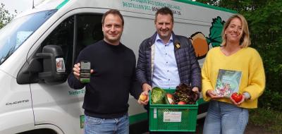 Drei Personen stehen vor einem Lieferwagen und halten Lebensmittel in die Kamera.