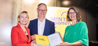 Drei Personen halten gemeinsam eine Urkunde in den Händen.