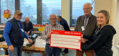 Vier Personen mit einem symbolischen Scheck in den Händen stehen in einer Werkstatt.