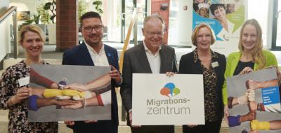 Fünf Personen stehen im Foyer eines Gebäudes vor einer Treppe.