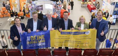 Sechs Personen mit einem Werbebanner in den Händen stehen auf der Empore einer Sporthalle.