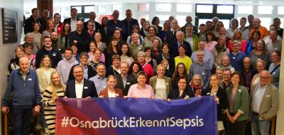 Eine große Personengruppe steht auf einer Treppe in einem Foyer.