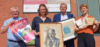 Vier Personen stehen vor einem Gebäude, an dem ein Banner hängt.