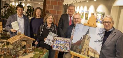Sechs Personen stehen neben einer Staffelei mit dem Foto einer Kirche.
