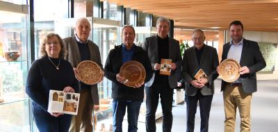 Sechs Personen mit Keramiktellern in den Händen stehen in einem Foyer vor Vitrinen.