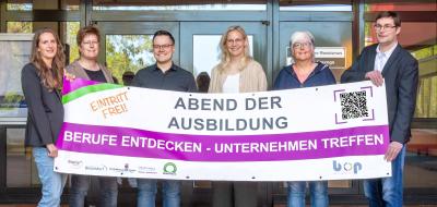 Sechs Personen mit einem Werbebanner in den Händen stehen vor einem Gebäudeeingang.