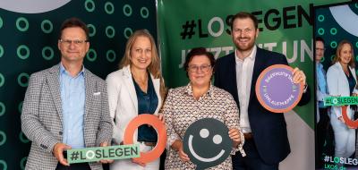 Vier Personen stehen vor einer Fotowand.