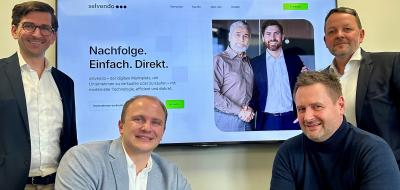 Vier Personen sitzen vor und stehen neben einem großen Bildschirm.