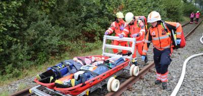 Drei Personen von Rettungsdiensten schieben eine Trage auf einer Schiene.