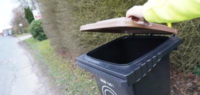 Person hebt den braunen Deckel einer Abfalltonne an.