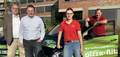 Vier Personen stehen neben dem Auto eines Pizzalieferdienstes.