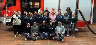 Eine Personengruppe steht vor einem Feuerwehrauto.