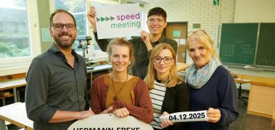 Fünf Personen stehen in einem Klassenraum.